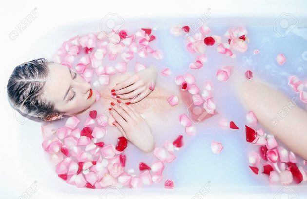 Young sexy girl taking a milk bath with rose petals closeup