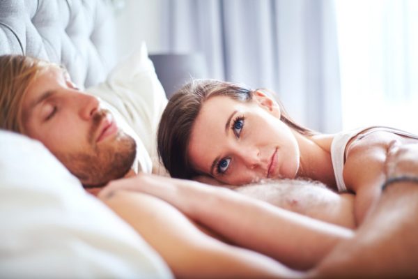 Pensive woman laying on sleeping man on bed