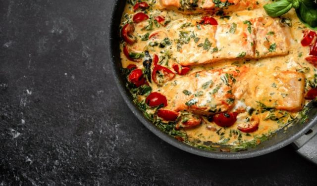 Close up of delicious tuscan cream salmon with spinach and cherry tomato in a pan on black background