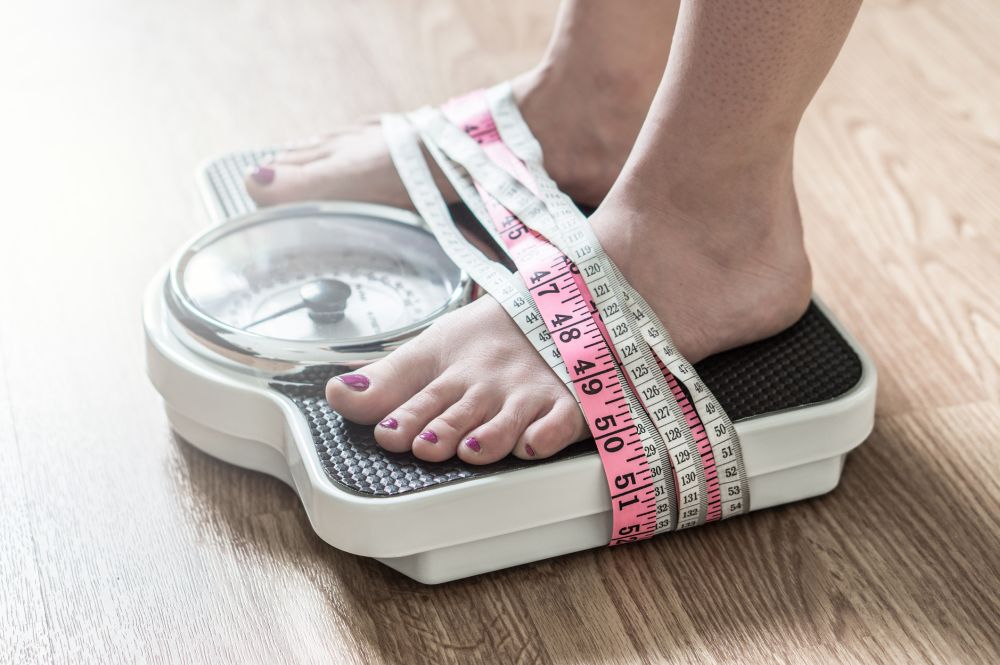 Anorexia and eating disorder concept. Feet tied up with measuring tape to a weight scale. Addiction and obsession to weight loss.