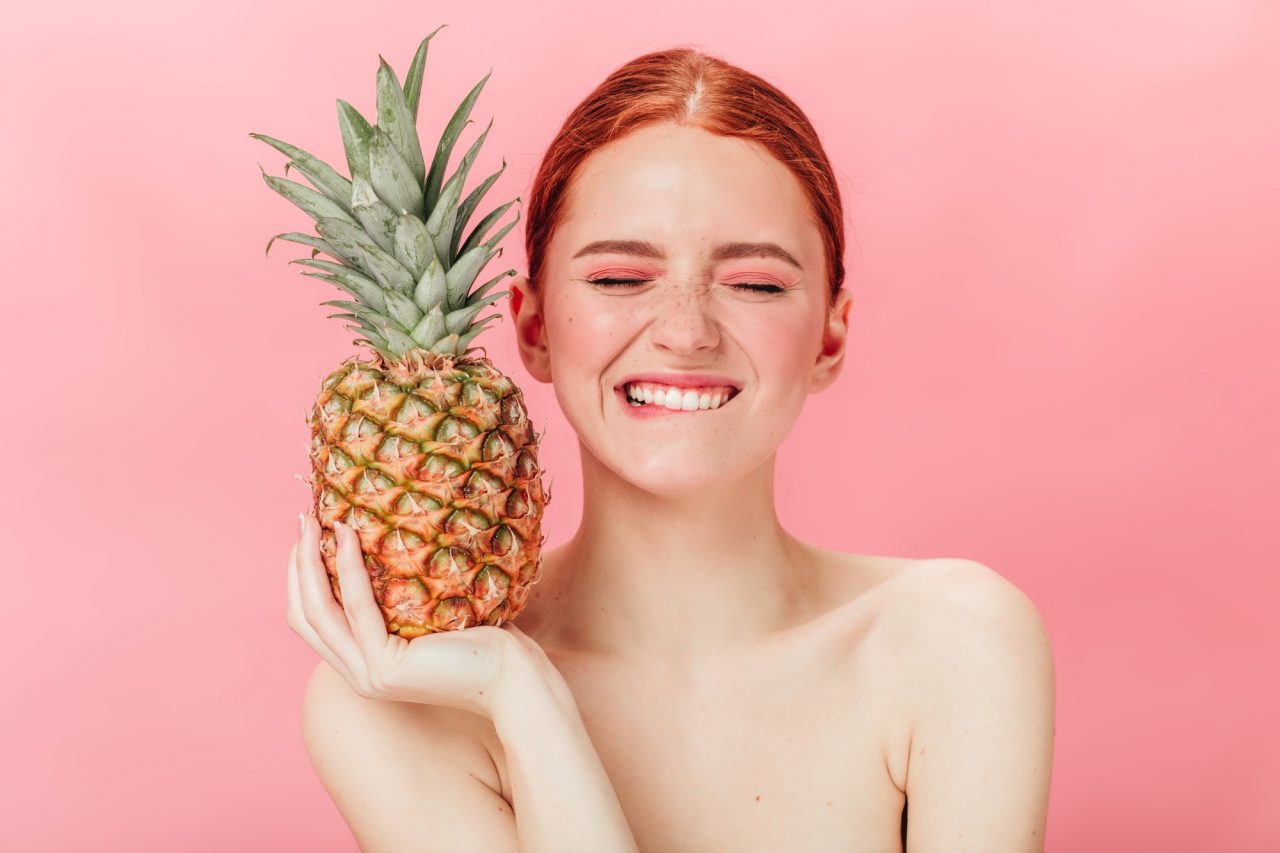 front-view-glad-woman-with-pineapple-posing-with-closed-eyes-studio-shot-excited-ginger-girl-holding-fruit-pink-background