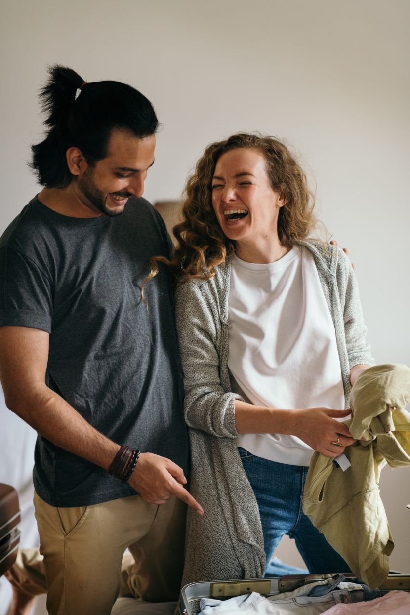 diverse-couple-laughing-while-packing-suitcases-for-holiday-4247722-830x0