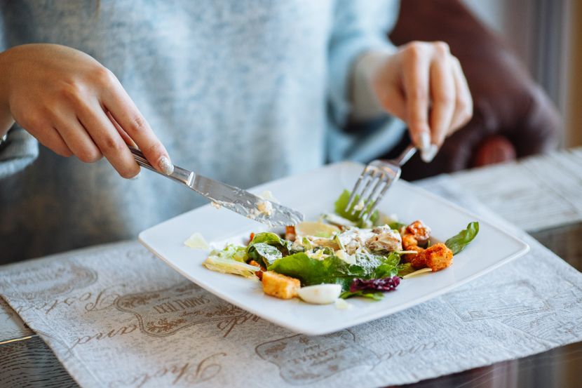 woman-s-hands-with-caesar-salad-table-restaurant-830x0