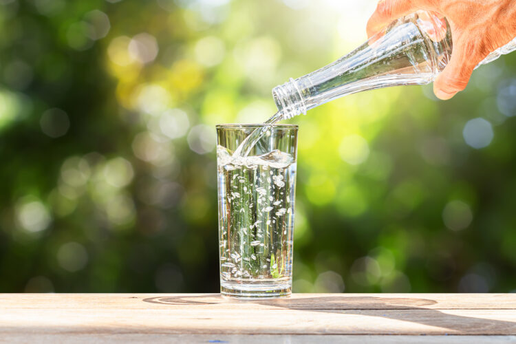 Hand,Holding,Drinking,Water,Bottle,Pouring,Into,Glass,On,Wooden