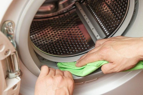 Hand cleaning moisture from the washing machine drum. Washing machine maintenance concept