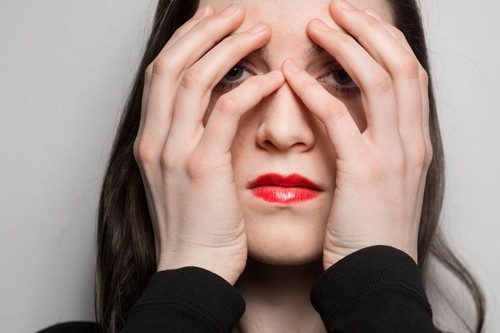 Young woman with hands covering face and red lipstick