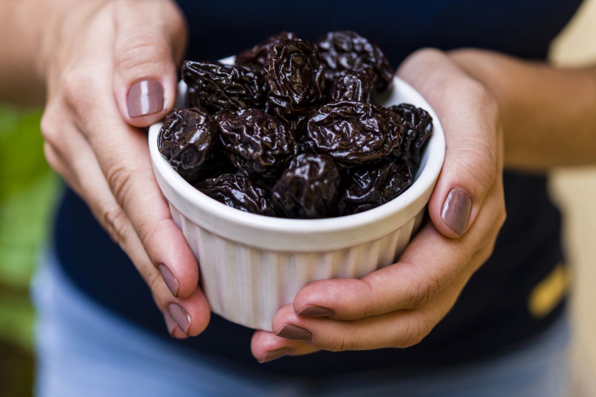 Hand of brunette model holding white pot with dried plum