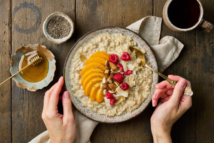 Oatmeal porridge with peach, raspberries, almond nuts, coconut chips, chia seeds, honey and tea