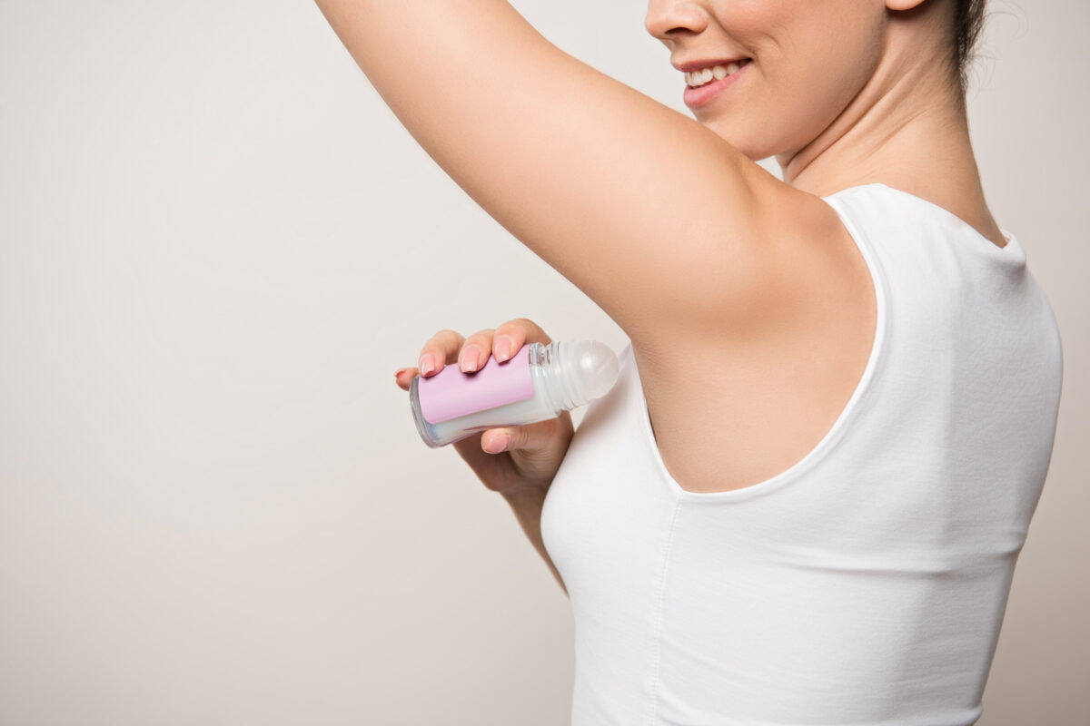 cropped view of smiling woman applying deodorant on underarm isolated on grey