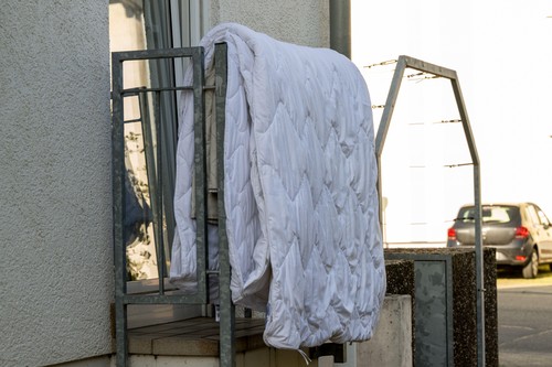 , Deutschland, 05.04.2025,  A white quilted blanket hangs over a metal railing on a balcony to air out. Everyday scene in a residential area during da