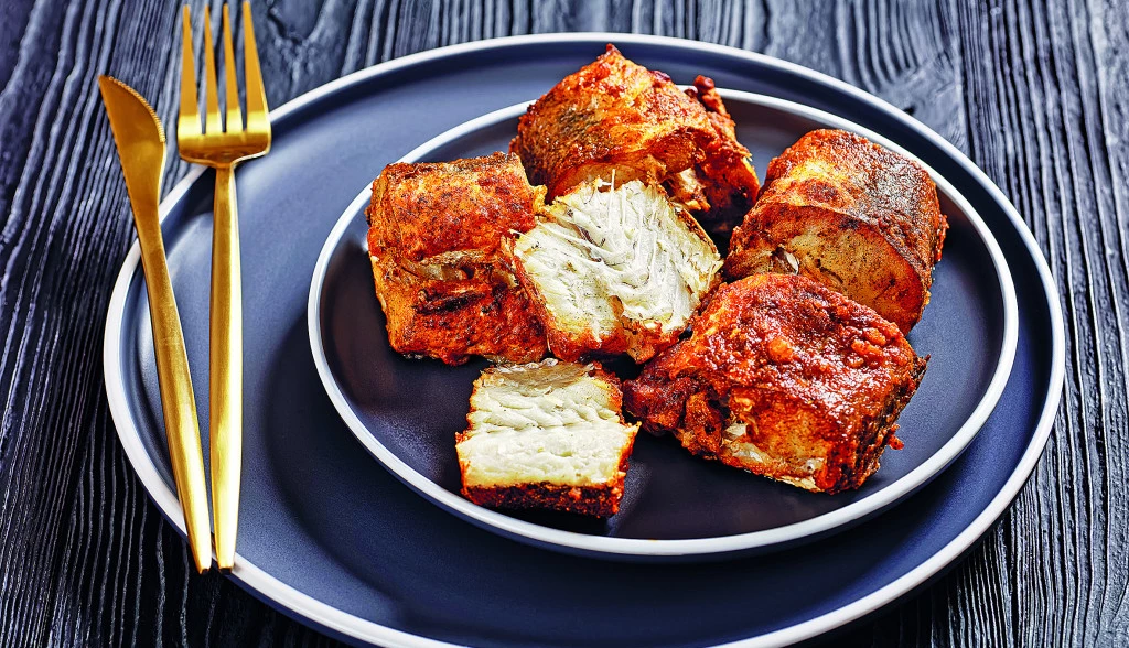 141561_pikantni-oslic-stock-photo-delicious-fried-pieces-of-hake-on-a-plate-with-golden-cutlery-on-a-black-wooden-table-close-up-2083023838_f.webp