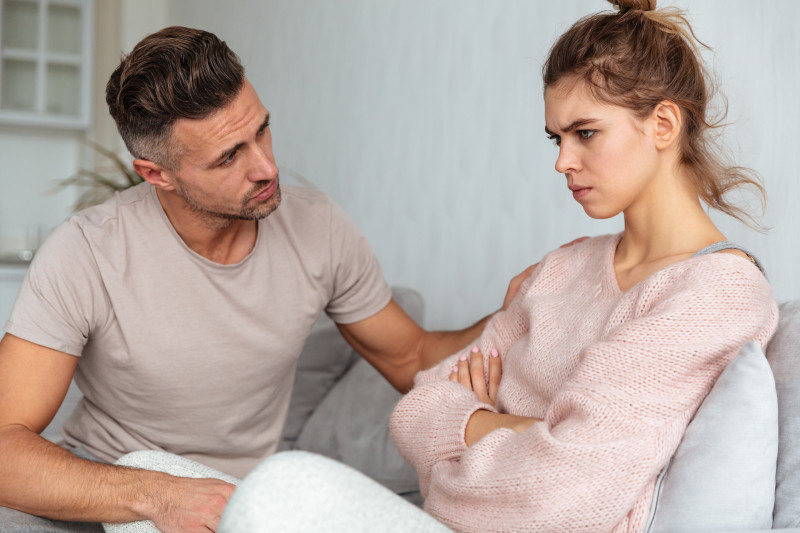 side-view-attentive-man-sitting-couch-calm-down-his-offended-girlfriend-home side-view-attentive-man-sitting-couch-calm-down-his-offended-girlfriend-home